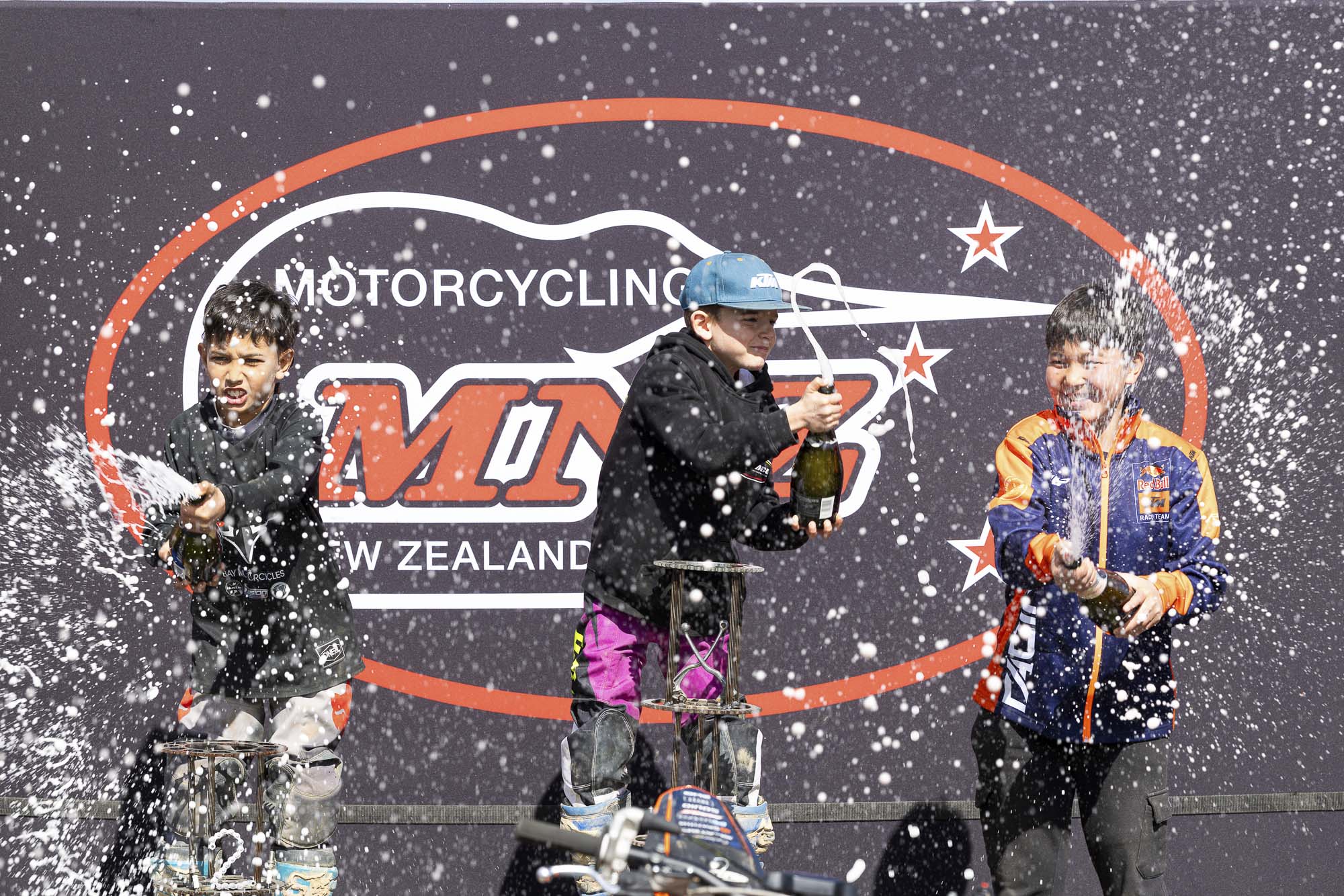 20261004-20261004_MiniMX_3561 The MX65 9-11 Years class podium celebrates with champagne (sparkling grape juice), from left: Dante McConnell (2nd), Royce Bush (1st) and Anand Rothe (3rd) at the 2026 NZ Mini Motocross Nationals