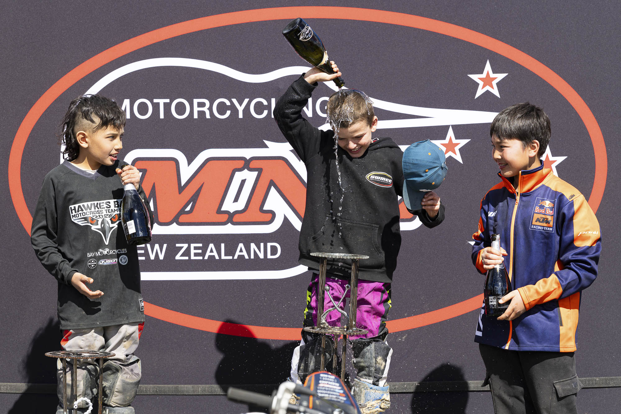 20261004-20261004_MiniMX_3607 The MX65 9-11 Years class podium celebrates with champagne (sparkling grape juice), from left: Dante McConnell (2nd), Royce Bush (1st) and Anand Rothe (3rd) at the 2026 NZ Mini Motocross Nationals