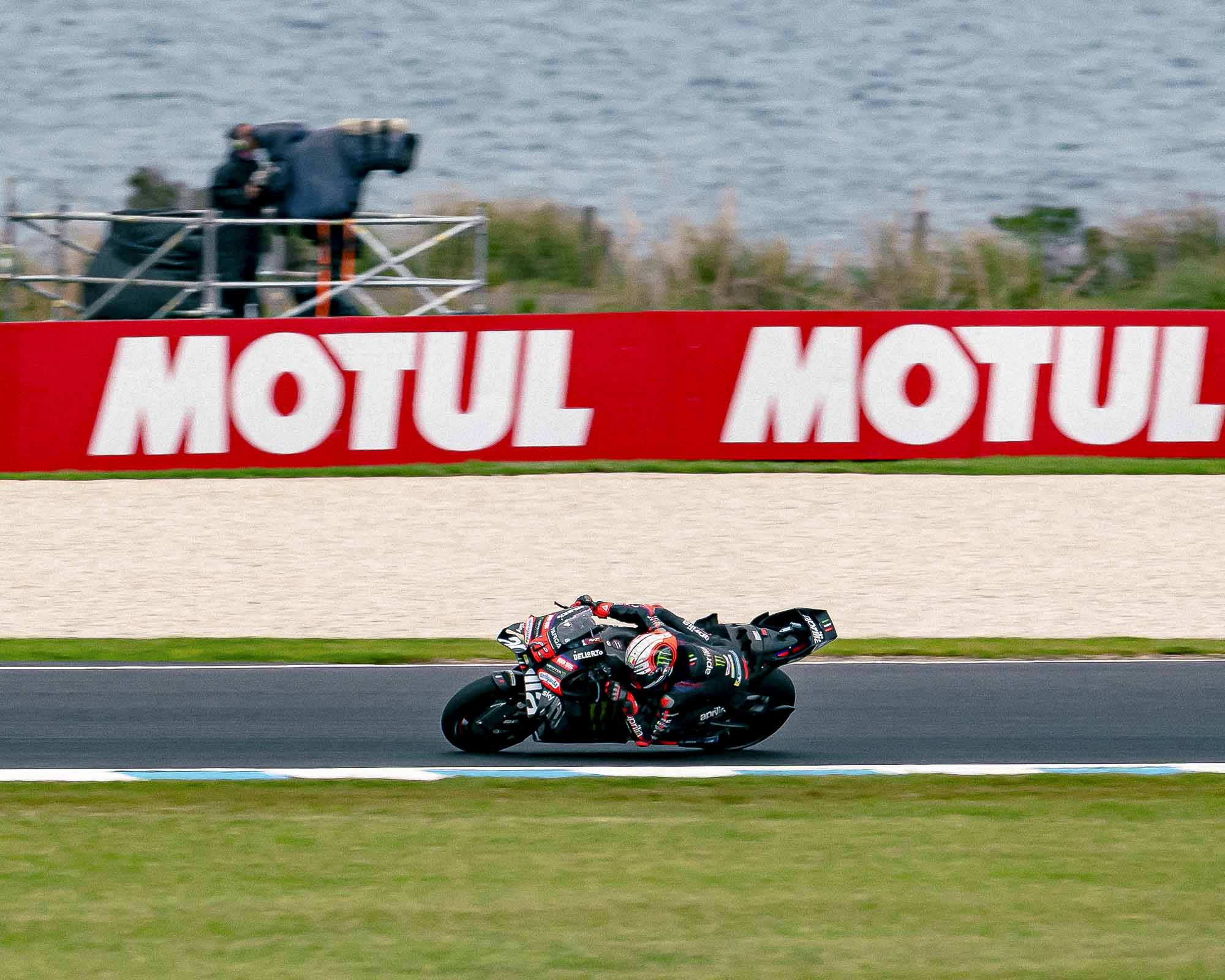 Aprilia MotoGP bike leaned into a corner at Phillip Island with the ocean behind.